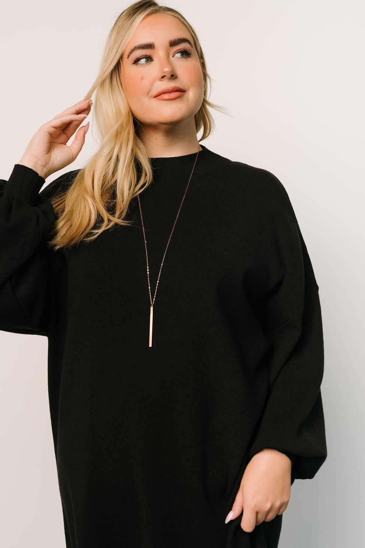 Styled flat-lay of the black sweater short dress folded to show knit texture, mock neckline, and bubble sleeve volume for product detail.